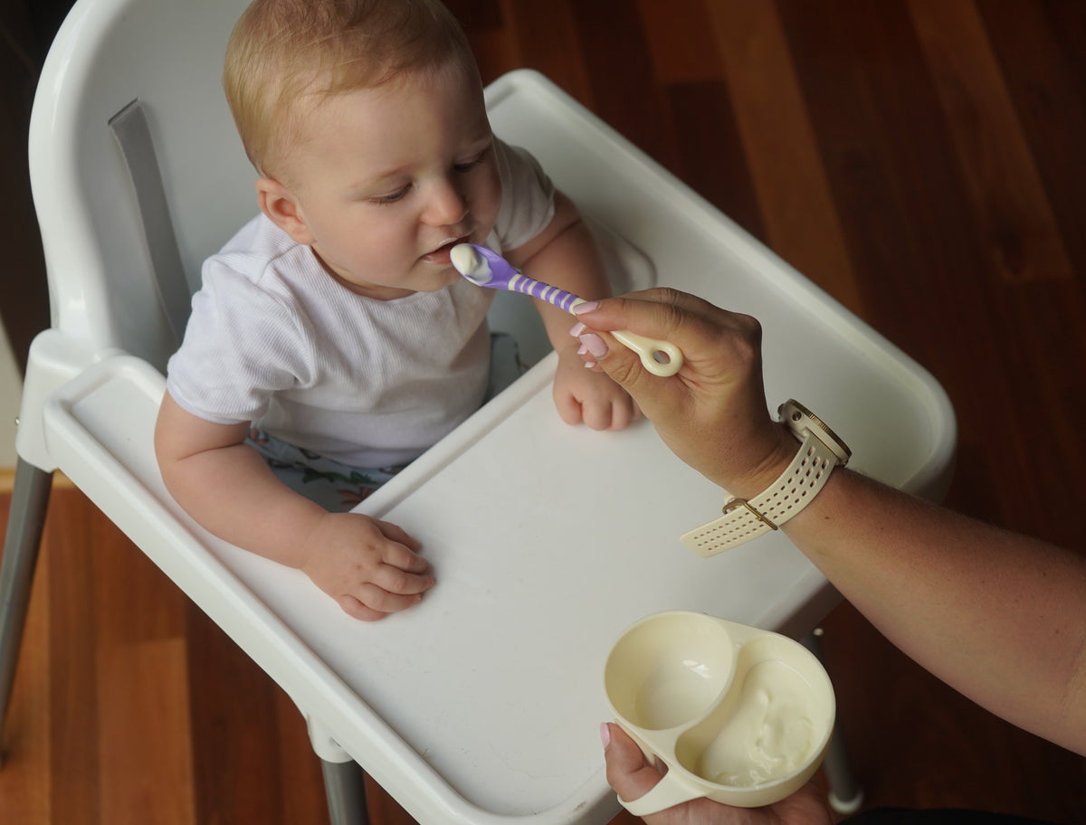 Baby being fed by mother with My First Solids Bowl and purple spoon