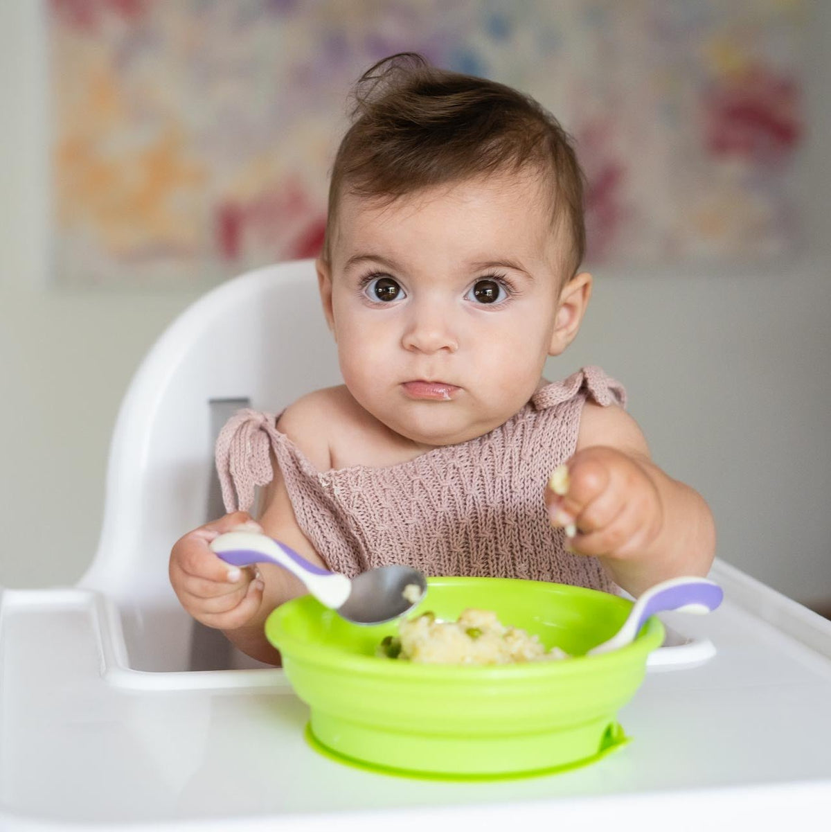 Baby using spoon and fork set with green bowl