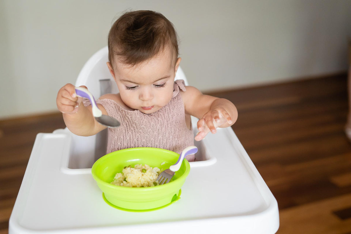 Baby using spoon and fork set with green bowl