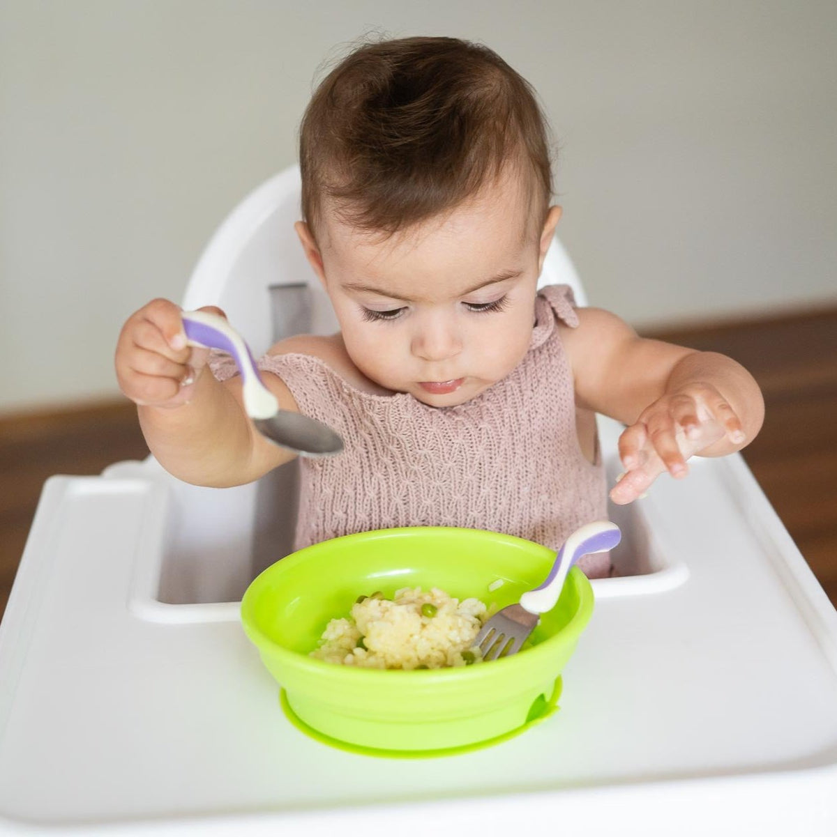 Baby using spoon and fork set with green bowl