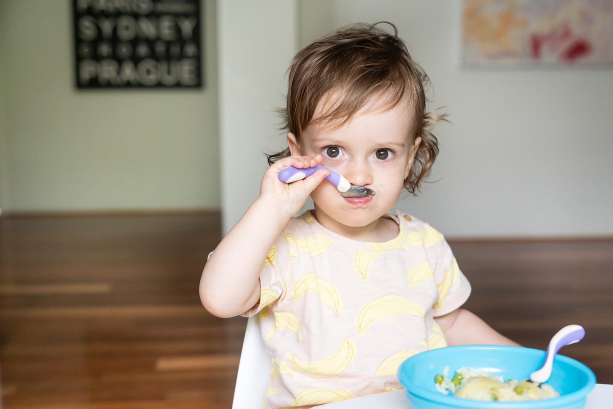 Toddler using spoon and fork set with aqua bowl