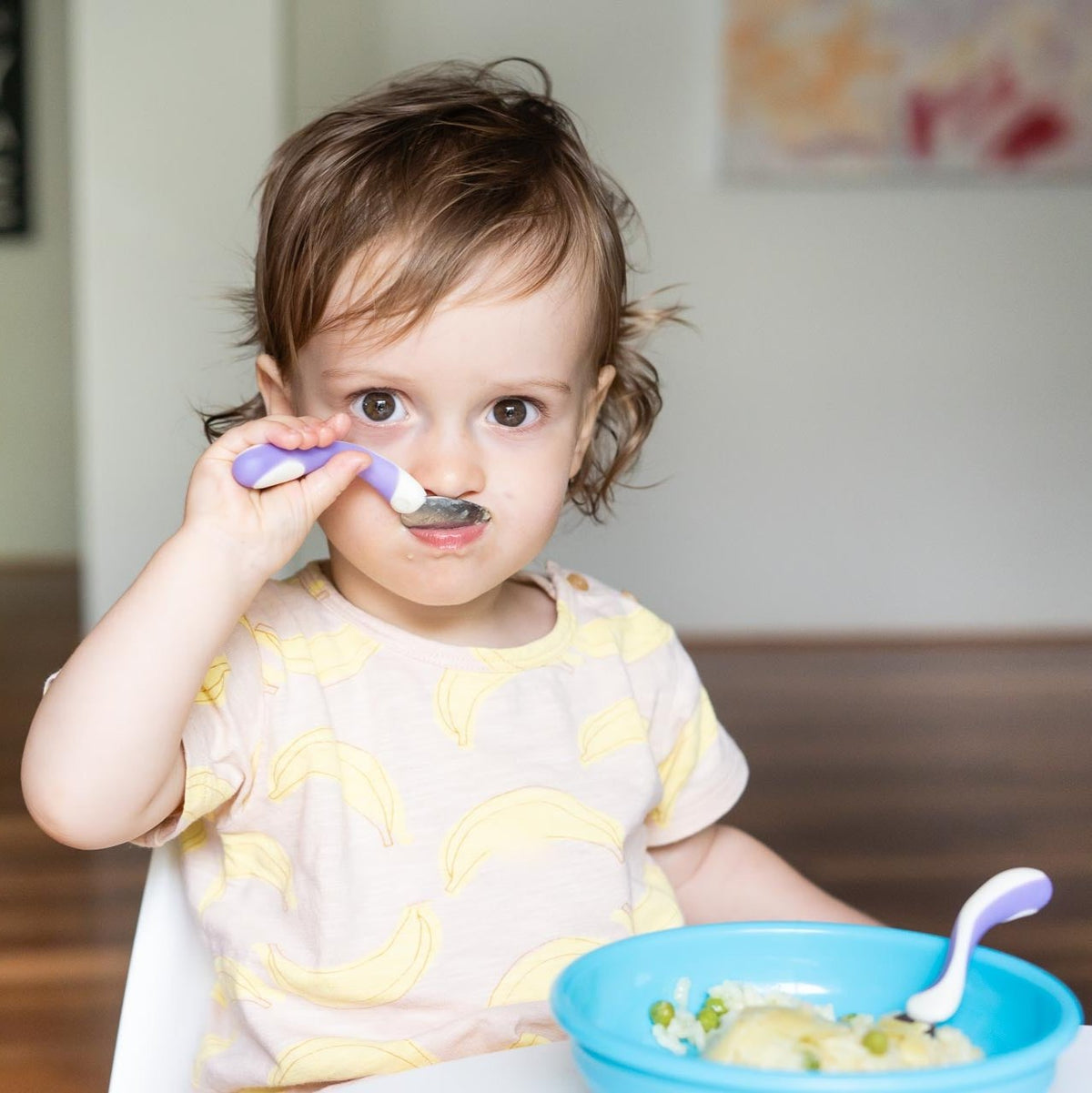 Toddler using spoon and fork set with aqua bowl